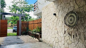 A modern outdoor entrance with a stone wall, wooden fence, and a concrete pathway leading to a vehicle. - Esha Tulum (Tulum)