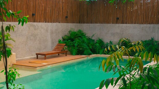 A swimming pool with a wooden deck and lounge chair, surrounded by lush greenery and a bamboo fence. - Esha Tulum (Tulum)