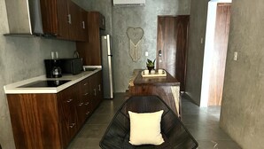 A modern kitchen with dark wooden cabinets, a stainless steel refrigerator, and a black chair with a white cushion. - Esha Tulum (Tulum)