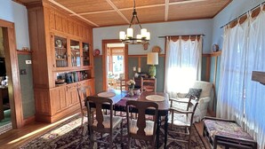 A dining area with a wooden table, chairs, and a patterned rug. There is a wooden cabinet with glass doors on the left, and a chair with a cushion on the right. - Colorful getaway in friendly Driftless village (Wonewoc)