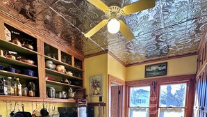 A kitchen with a stove, oven, and various kitchen utensils. There is a window with curtains, a ceiling fan, and a green rug. - Colorful getaway in friendly Driftless village (Wonewoc)
