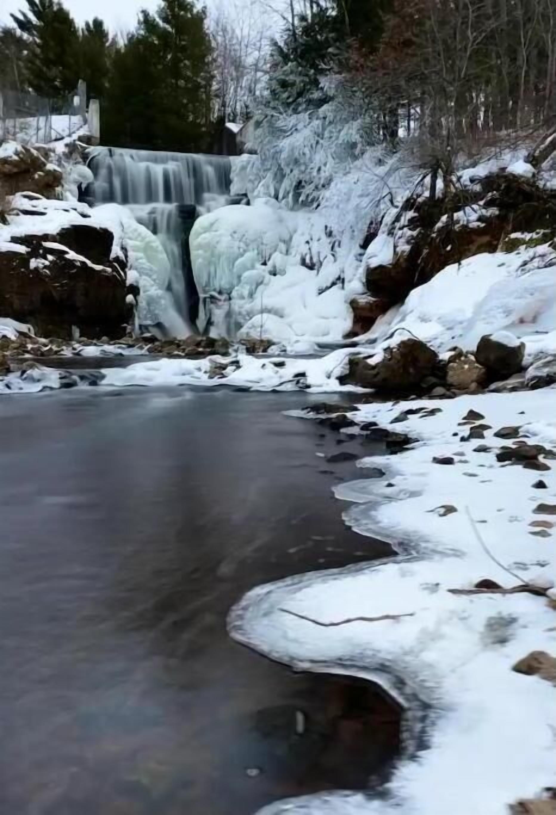 A waterfall with snow-covered rocks and a frozen stream.