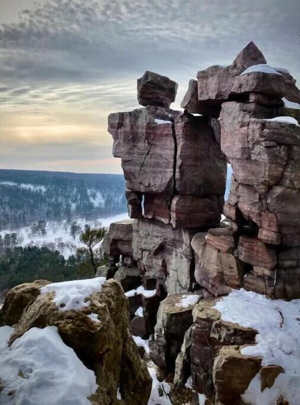 A rocky outcrop with a snow-covered foreground and a forested valley in the background.