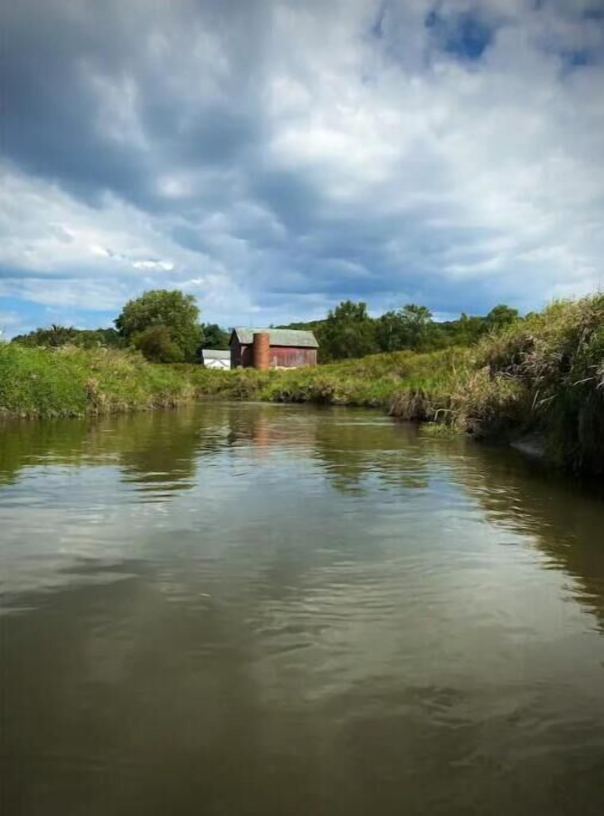 Une rivière paisible, avec un bâtiment rouge sur la rive opposée.