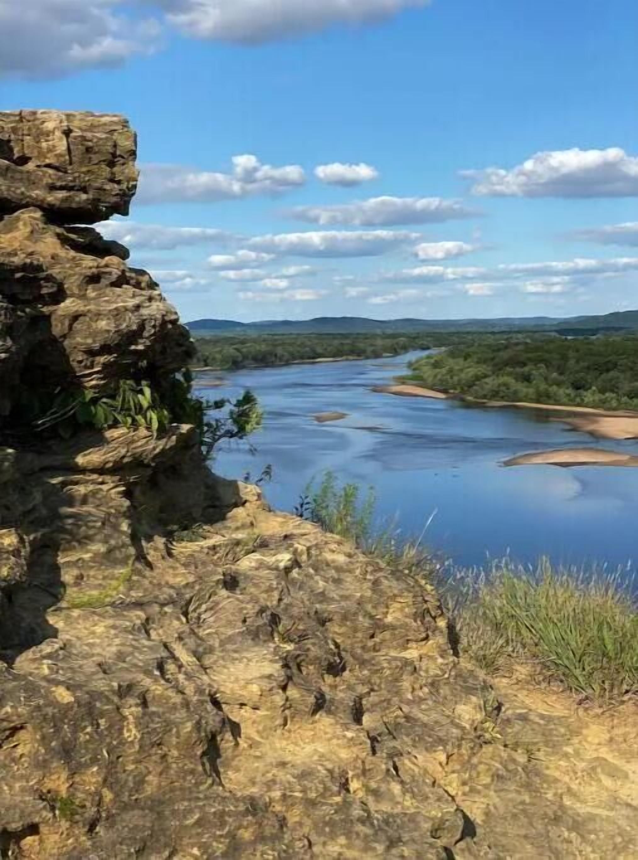 Een rotsachtige klif met uitzicht op een rivier, onder een heldere lucht.