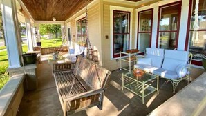 A covered porch with a wooden bench, a glass table, and white cushioned chairs. - Colorful getaway in friendly Driftless village (Wonewoc)