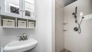 A bathroom with a white sink, wicker baskets on shelves, and a shower area with tiled walls. - Studio 01 - Lake Sumner (Clermont)