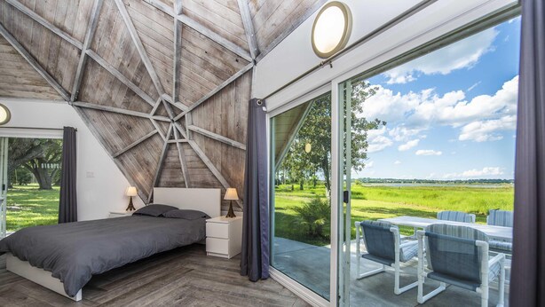 A bedroom with a large window, wooden ceiling, and a view of a green landscape. - Studio 01 - Lake Sumner (Clermont)