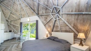 A bedroom with a large bed, a nightstand with a lamp, and a view of the outdoors through a glass door. - Studio 01 - Lake Sumner (Clermont)