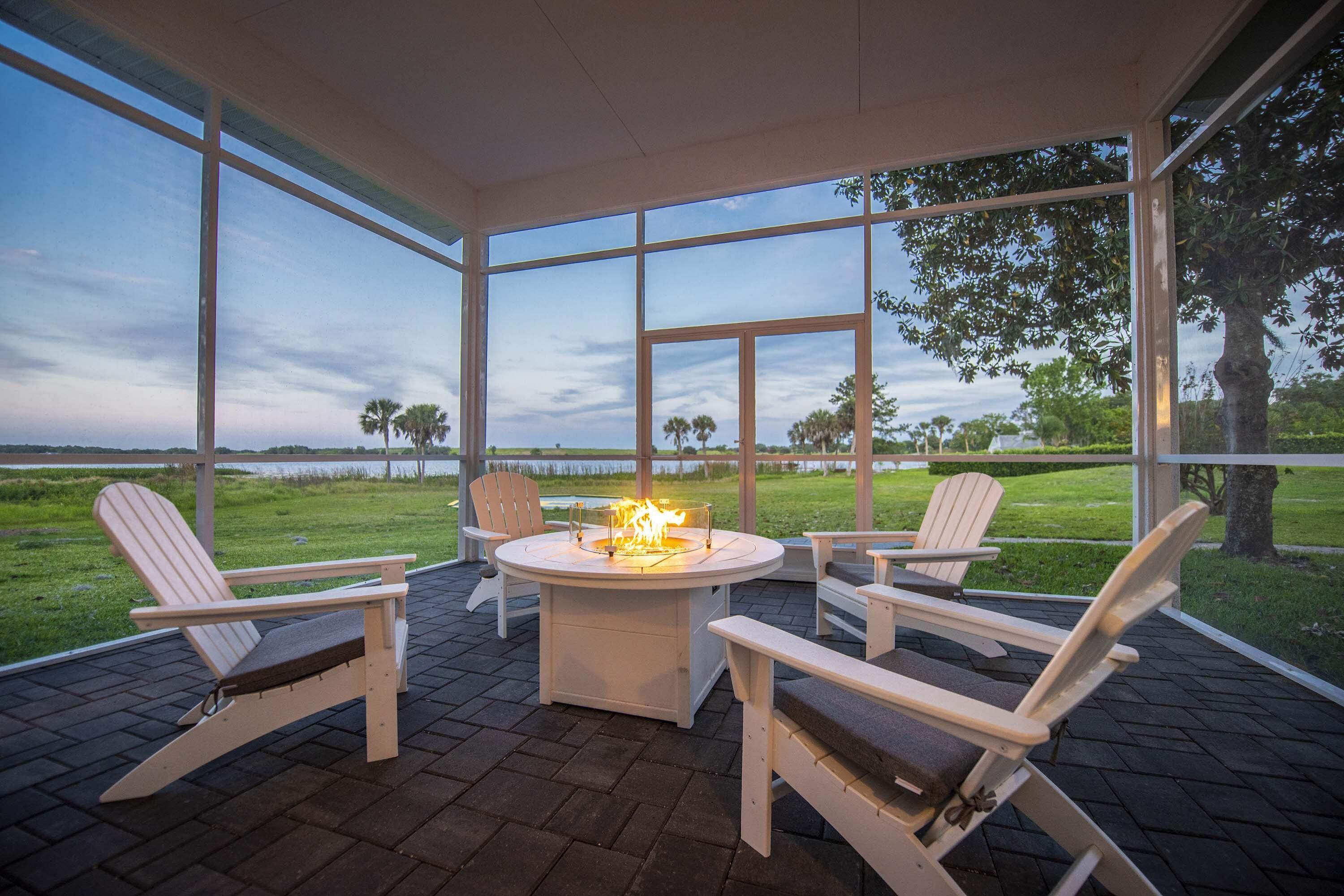 Portico coperto con poltrone Adirondack, un elemento centrale a forma di focolare e vista su un prato e alberi.