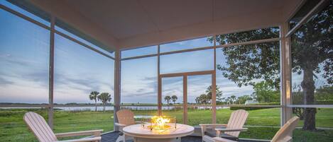 Portico coperto con poltrone Adirondack, un elemento centrale a forma di focolare e vista su un prato e alberi.
