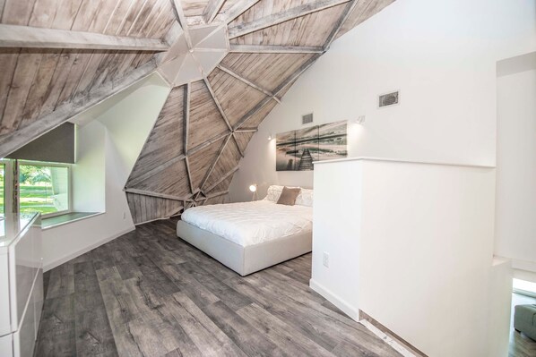Un dormitorio con techo inclinado, una cama, una mesita de noche y una ventana.