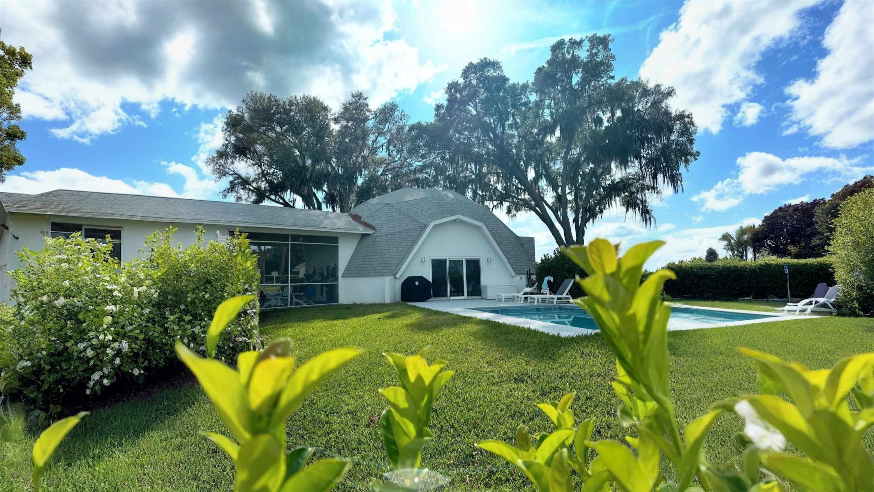 Une maison moderne dotée d’une grande pelouse, d’une piscine et d’un patio couvert.