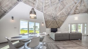 Un loft spacieux avec de hauts plafonds, un coin repas doté de chaises modernes, un canapé gris et de grandes fenêtres offrant une vue sur l’extérieur.