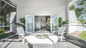 Une terrasse couverte avec une table ronde et deux chaises blanches, une table basse en verre et des plantes en pot.