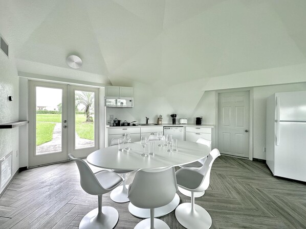 A modern kitchen with white cabinets, a dining table with four chairs, and a large window overlooking a garden. - Sumner Lake Tiny House - Lake Sumner (Clermont)