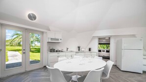 A modern kitchen with a white dining area, large windows, and a view of greenery. - Sumner Lake Tiny House - Lake Sumner (Clermont)