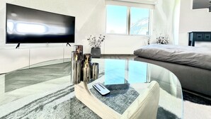 A modern bedroom with a TV, a glass coffee table, a bed, and a window. - Sumner Lake Tiny House - Lake Sumner (Clermont)