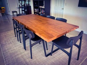 Uma mesa retangular de madeira com seis cadeiras, uma estante e uma porta em um quarto com carpete.