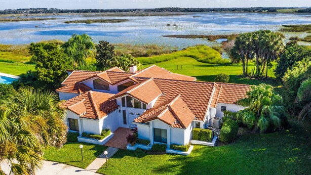 A large house with a red-tiled roof, surrounded by lush greenery and a body of water. - Swiss 06 - Lake Sumner (Clermont)