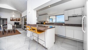 A modern kitchen with white cabinetry, a granite countertop, and a bar area with stools. - Swiss 06 - Lake Sumner (Clermont)