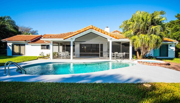 A modern house with a swimming pool, a covered patio, and a well-maintained lawn.