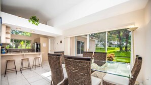 A modern kitchen with a bar area, wicker chairs, and a glass dining table. - Swiss 101 - Lake Olsen (Clermont)