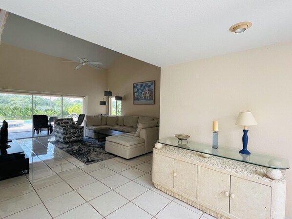A spacious living room with a large sectional sofa, a glass coffee table, and a dining area with chairs.