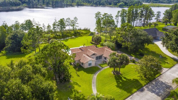 A large house with a red-tiled roof, surrounded by lush green lawns and tall trees, with a lake in the background. - Swiss 101 - Lake Olsen (Clermont)