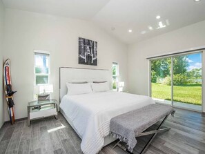 Une chambre moderne avec un grand lit, un porte-skis et une vue sur un paysage verdoyant, visible à travers une porte-fenêtre coulissante.