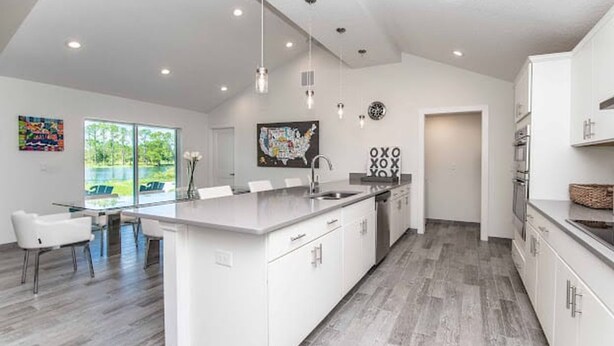 Uma cozinha moderna com uma ilha grande, armários brancos e uma área de jantar com mesa e cadeiras.