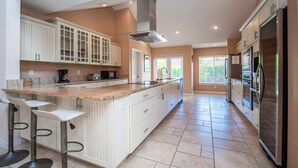 A spacious kitchen with white cabinetry, a large island with bar stools, stainless steel appliances, and a view to the outside. - Swiss 105 - Lake Olsen (Clermont)