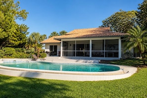 Una casa con piscina, patio cubierto y césped.
