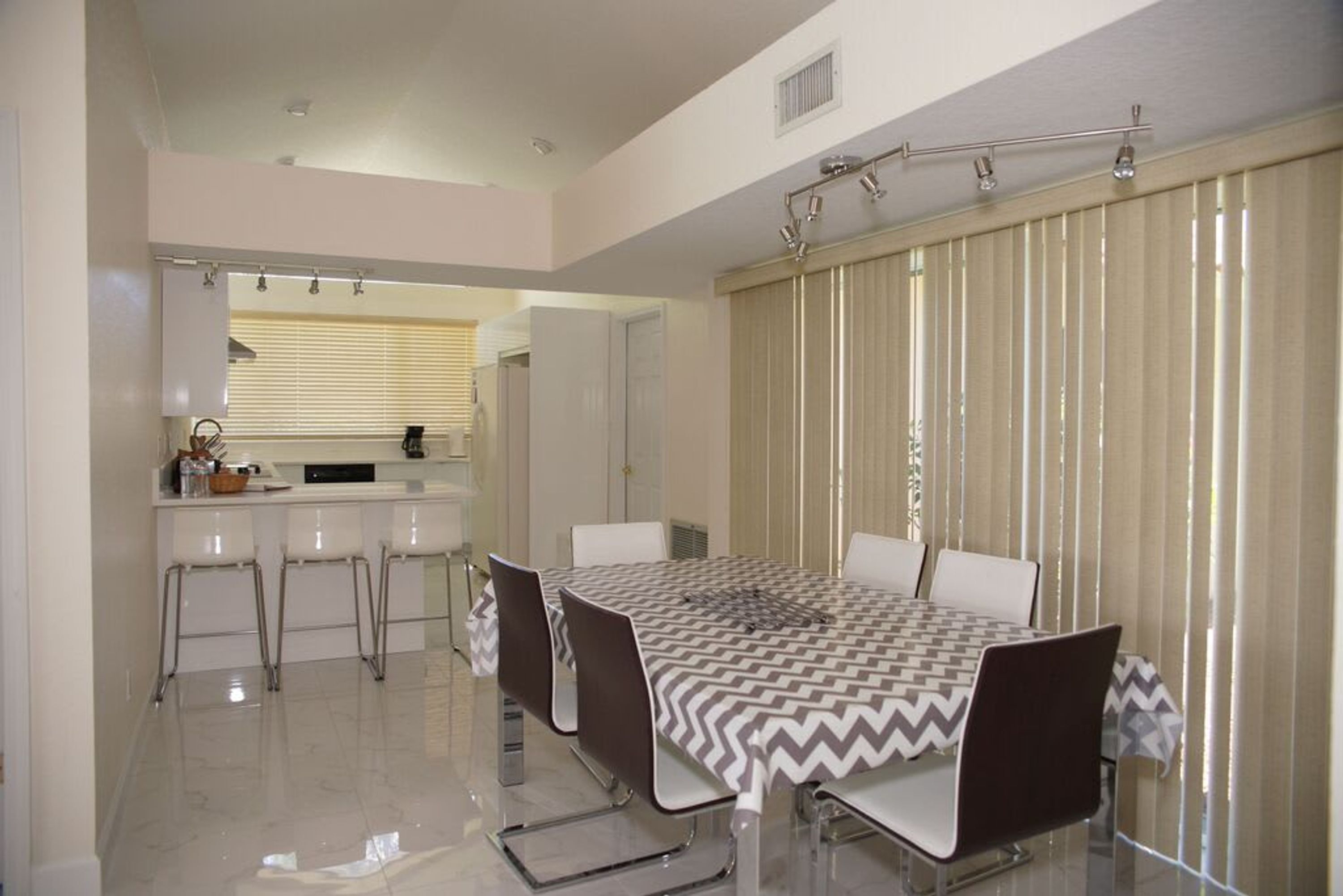 A modern dining area with a large table, white chairs, and a kitchen in the background.