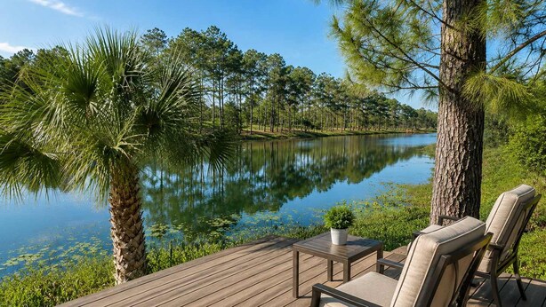 Une terrasse en bois avec des meubles d’extérieur, un lac paisible et des arbres tout autour.