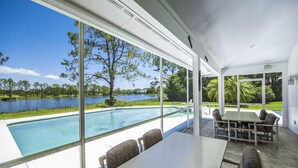 A poolside area with a table and chairs, large windows offering a view of a lake and trees. - Swiss 23 - Lake Stephanie (Clermont)