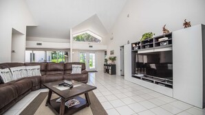 A spacious living room with a brown leather sofa, a coffee table, and a large flat-screen TV. There is a bookshelf with decorative items and a potted plant. - Swiss 23 - Lake Stephanie (Clermont)