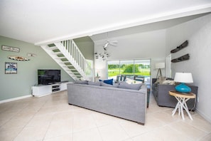 A spacious living room with a grey sofa, a television, and a staircase leading to another level.