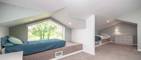A bedroom with a sloped ceiling, a window, a bed, a dresser, and a nightstand.