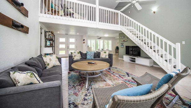 A spacious living area with a high ceiling, a white staircase, a round coffee table, and a large TV. - Swiss 31 - Golf Course (Clermont)