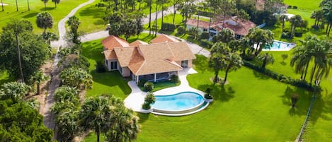 A large house with a swimming pool surrounded by well-maintained lawns and palm trees.