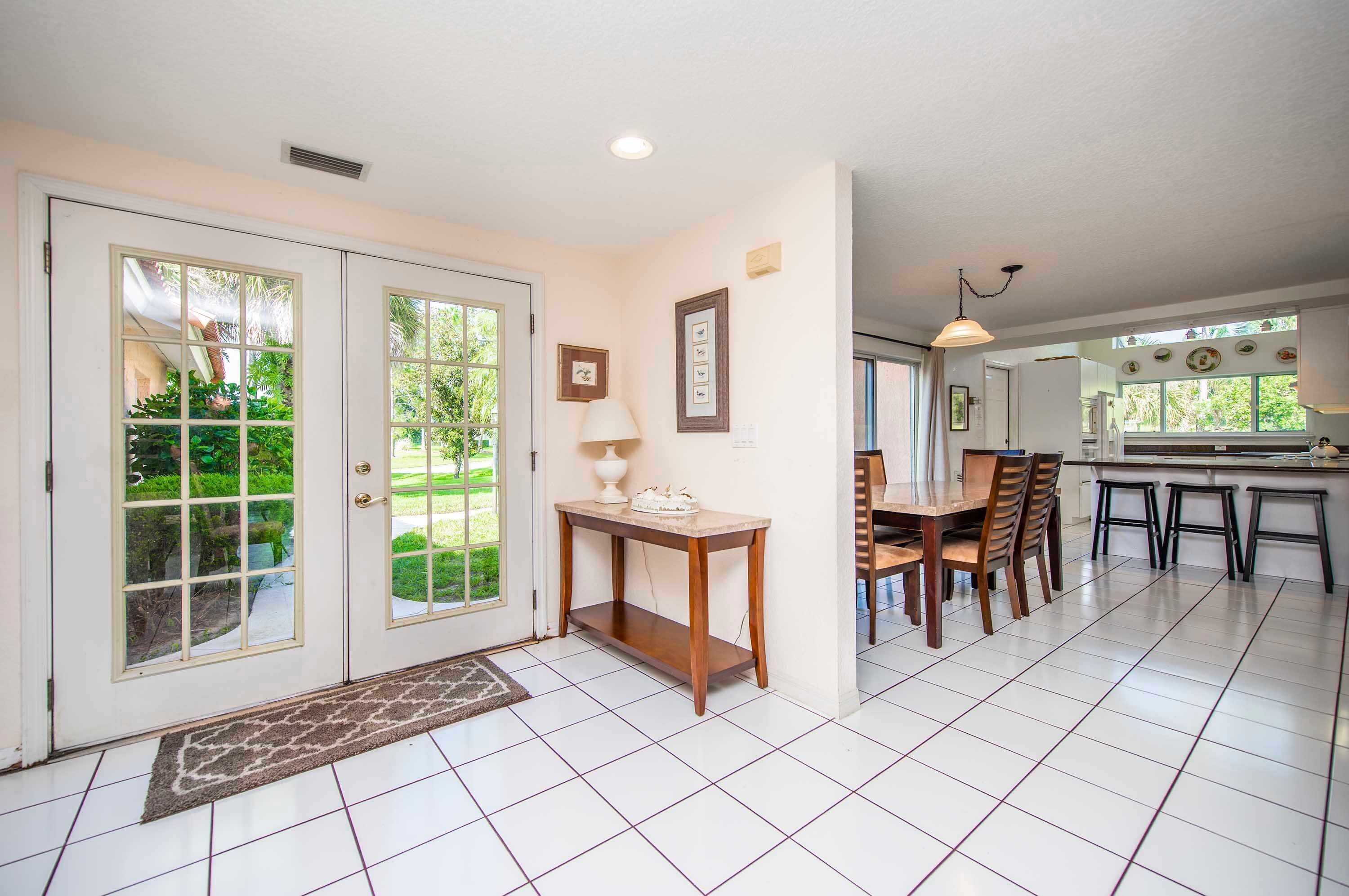 A spacious kitchen with a dining area, white tiled flooring, and a view of the outdoors.