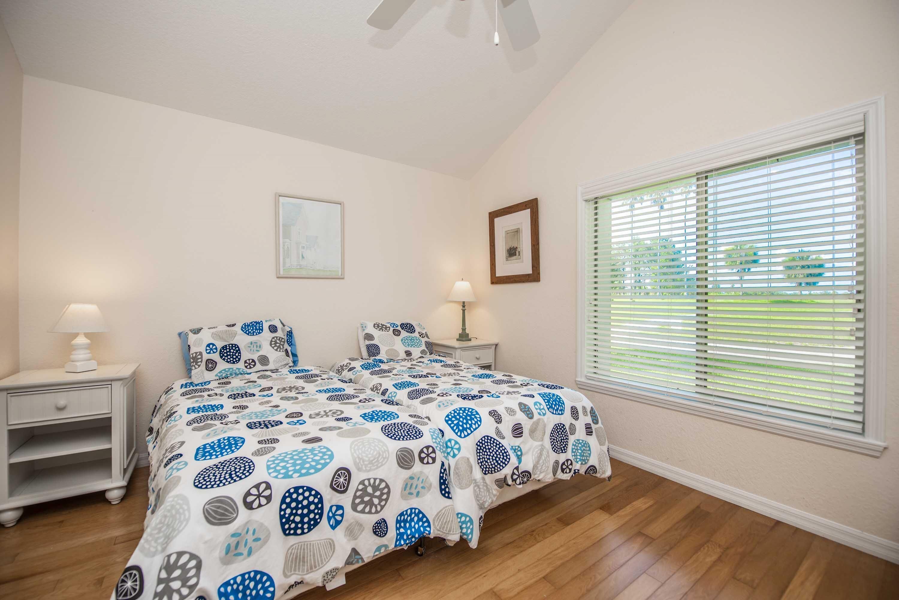A bedroom with a bed, two bedside tables, a ceiling fan, and a window with blinds.