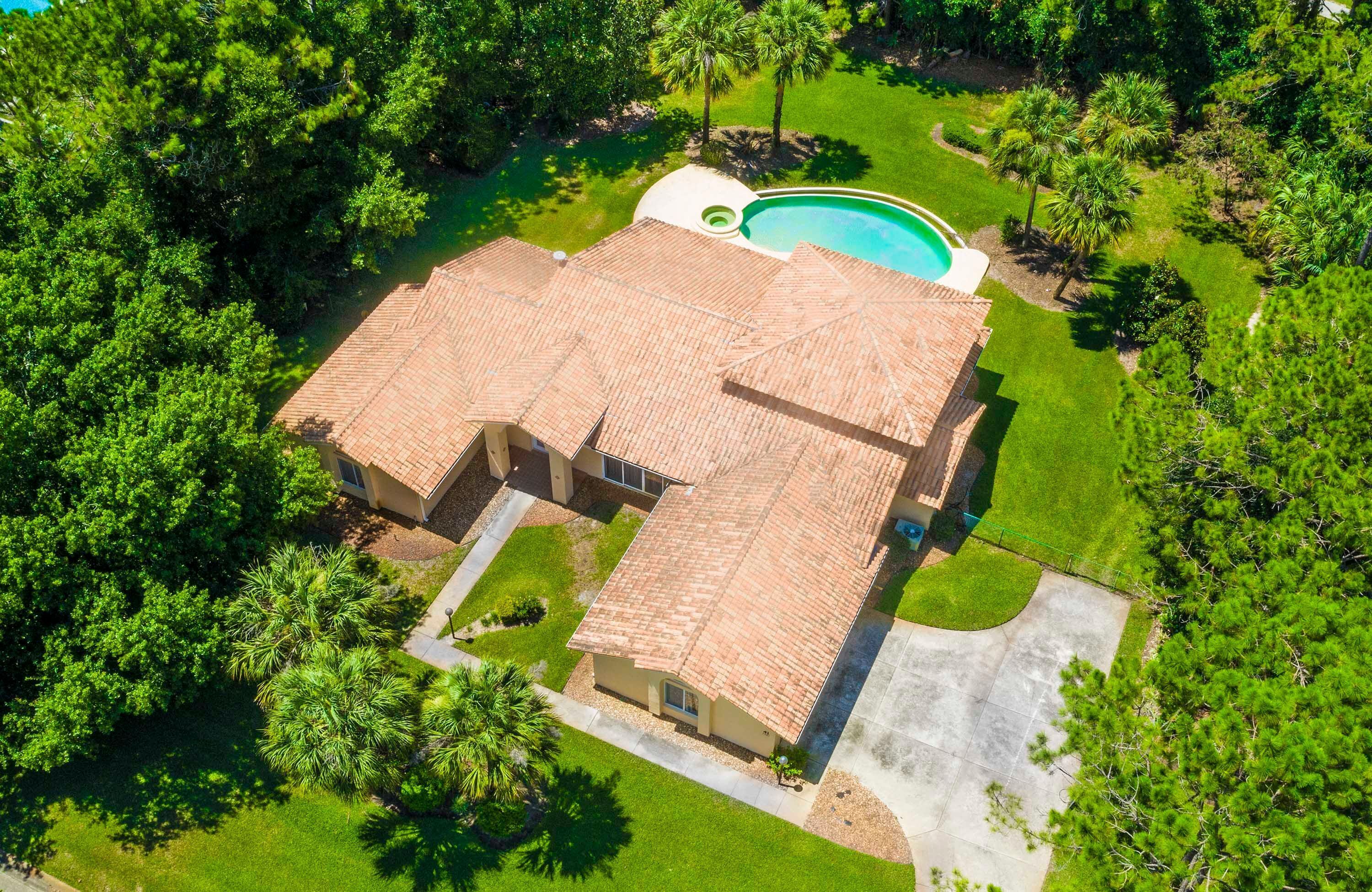 An aerial view of a house with a swimming pool, surrounded by lush greenery.