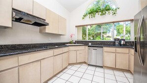 A modern kitchen with light-colored cabinets, a black countertop, and a window with a view of trees. - Swiss 41 - Golf Course (Clermont)