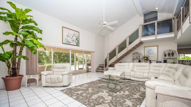 A spacious living room with a large potted plant, white sofas, a glass coffee table, and a staircase leading to an upper level. - Swiss 41 - Golf Course (Clermont)