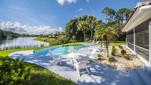 Piscina com espreguiçadeiras, cercada por vegetação e vista para um lago.