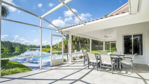 Alpendre coberto com vista para um lago e piscina, mobiliário de exterior e ventoinha no teto.