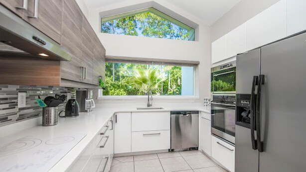 Uma cozinha moderna com armários brancos, eletrodomésticos de aço inoxidável e uma janela ampla com vista para o verde.