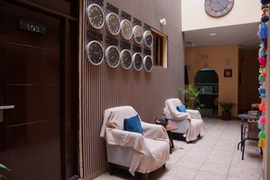 A lobby with multiple clocks displaying different time zones, a reception desk, and two lounge chairs. - Posada Miraflores (Lima)